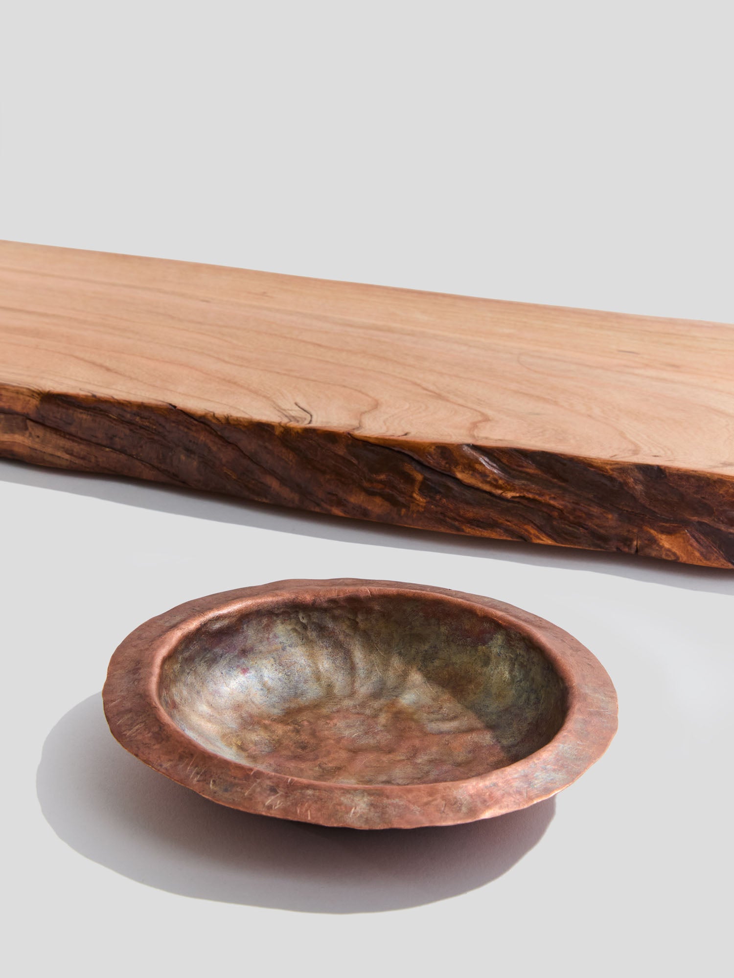  close up of live-edge cherry wood bath tray and a hand-hammered copper ashtray