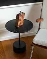 Small black side table with a wooden lighter on it, next to a chair with a white cushion.