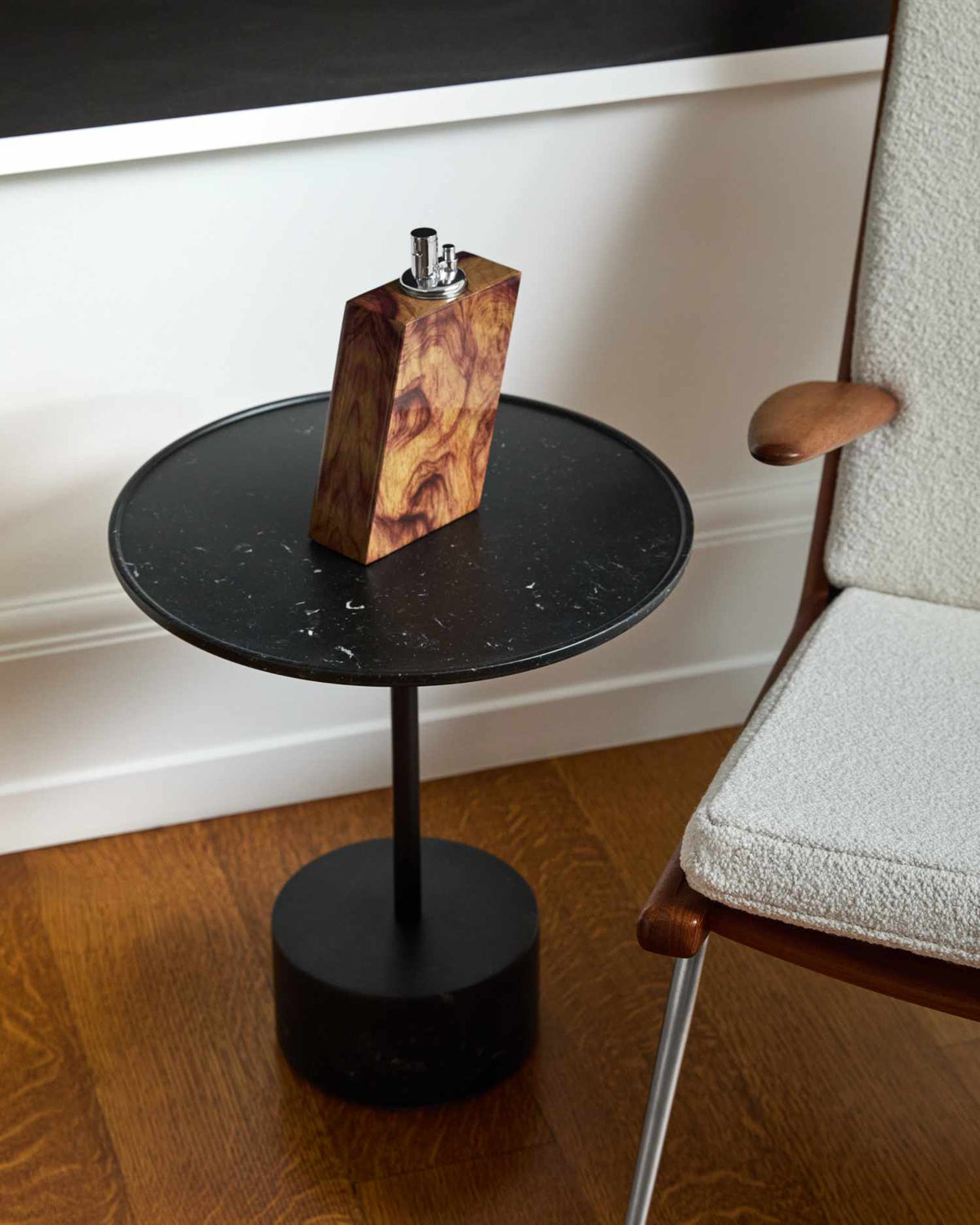 Small black side table with a wooden lighter on it, next to a chair with a white cushion.